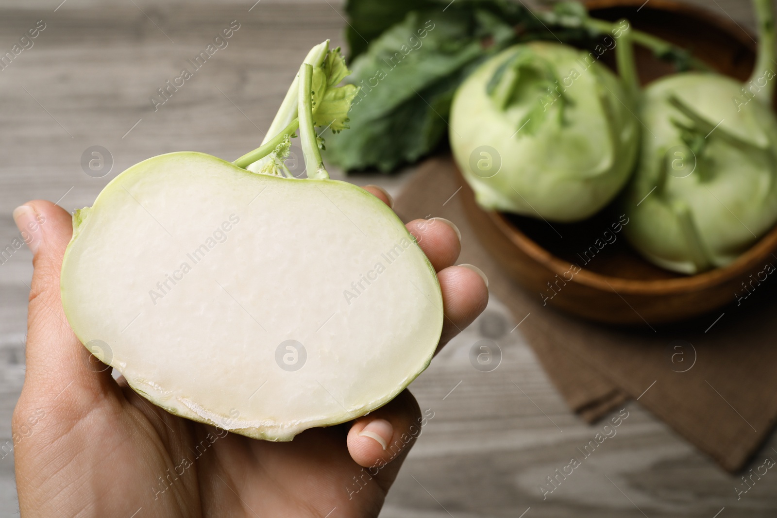 Photo of Woman holding half of kohlrabi plant at table, closeup