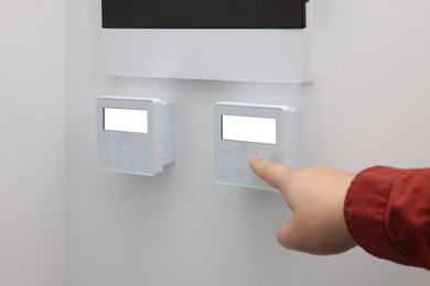 Photo of Man adjusting thermostat on white wall, closeup. Smart home system