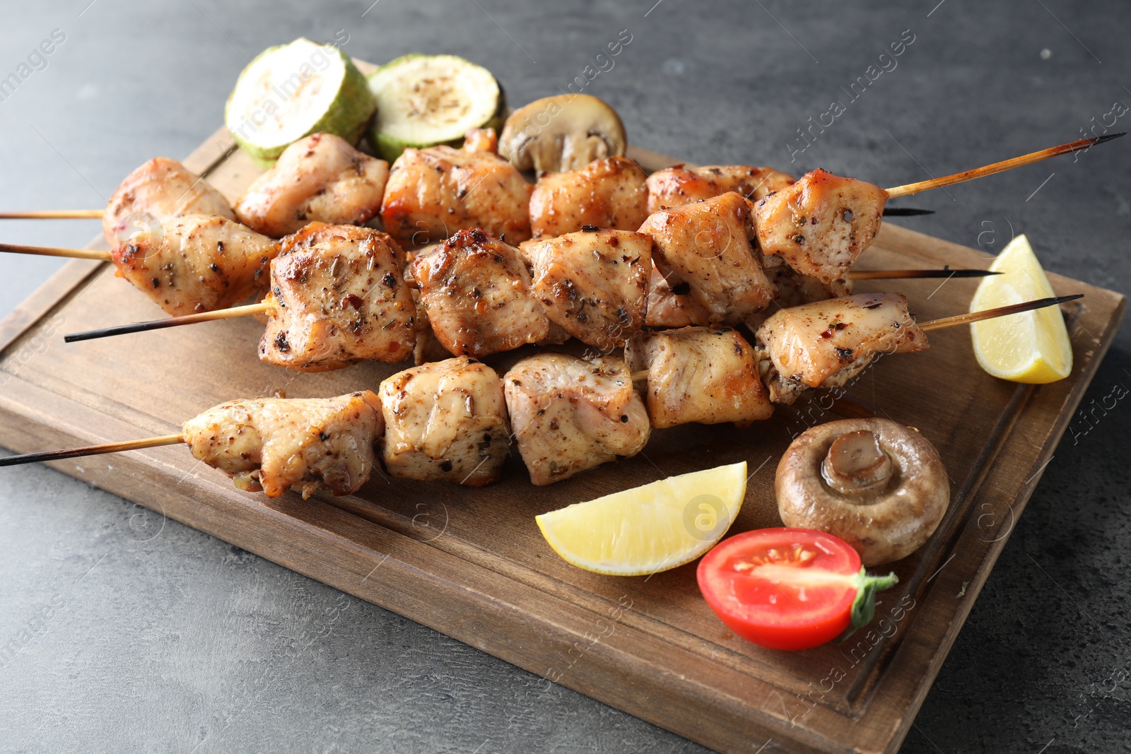Photo of Delicious shish kebabs with vegetables and lemon on grey table
