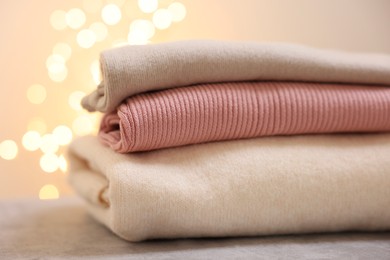 Stack of folded clothes on grey table against blurred lights, closeup