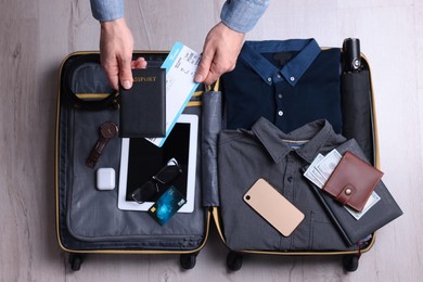 Photo of Man packing suitcase for business trip on wooden floor, top view