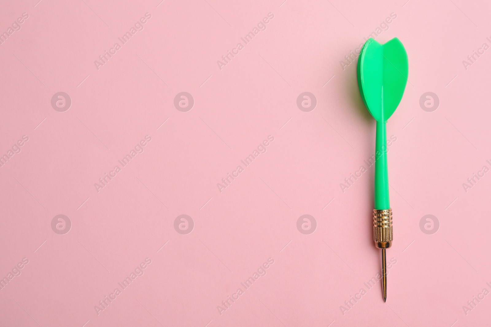 Photo of Green dart arrow on pink background, top view with space for text