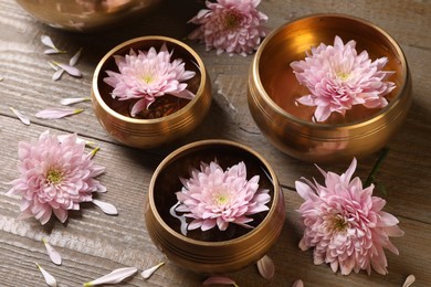 Tibetan singing bowls with water and beautiful flowers on wooden table