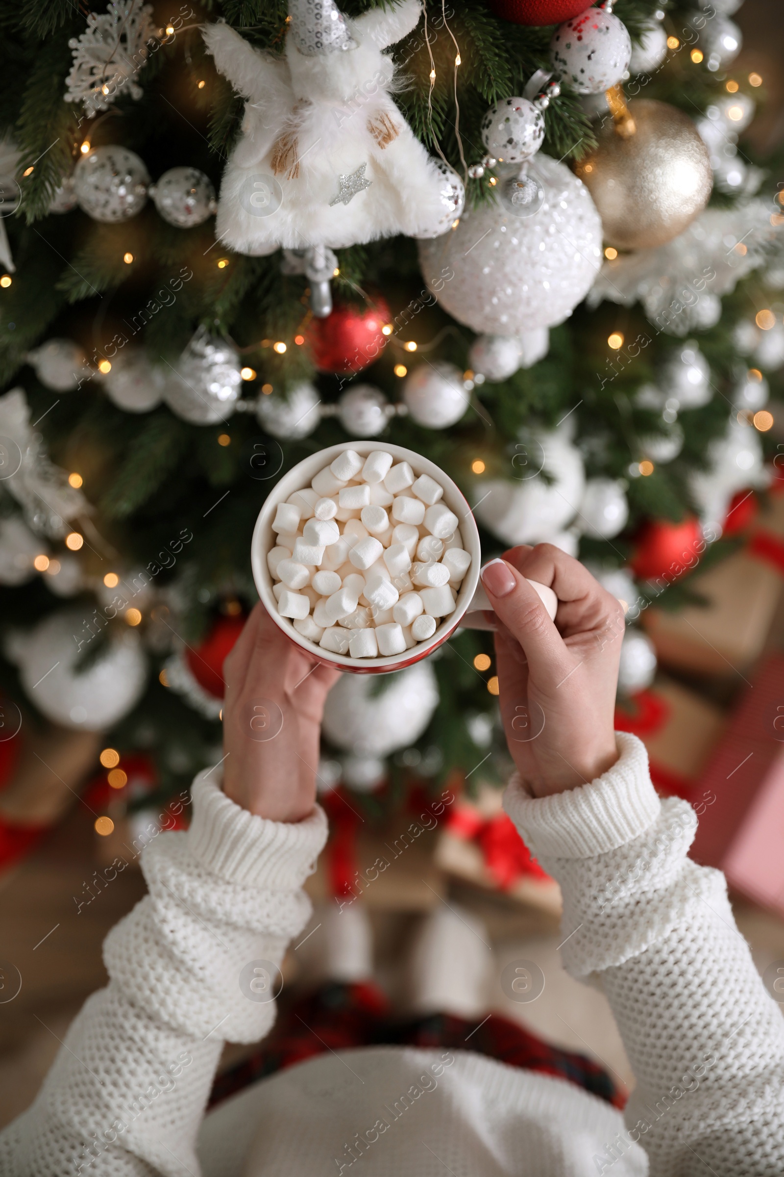 Photo of Woman with cup of delicious hot drink near Christmas tree at home, top view