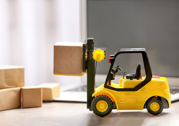 Photo of Toy forklift with box near laptop on table. Logistics and wholesale concept