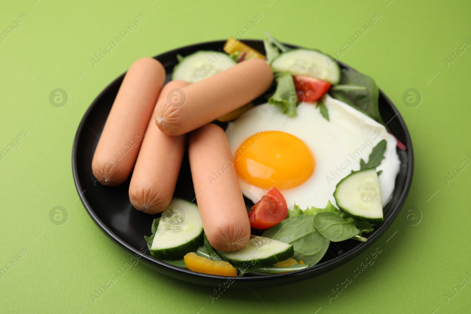 Photo of Delicious breakfast with boiled sausages and fried egg on green background