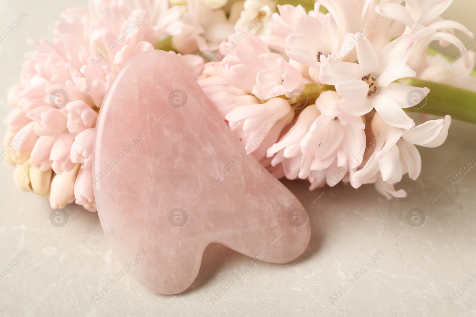 Photo of Rose quartz gua sha tool and hyacinth flower on grey table, closeup