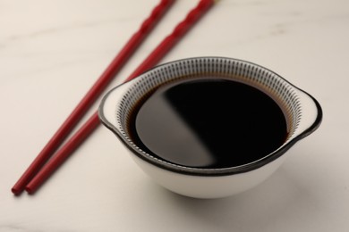 Photo of Bowl with soy sauce and chopsticks on white table, closeup