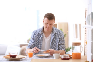Photo of Young man spreading jam onto tasty toasted bread at table