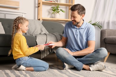 Photo of Happy man receiving greeting card from his little daughter at home