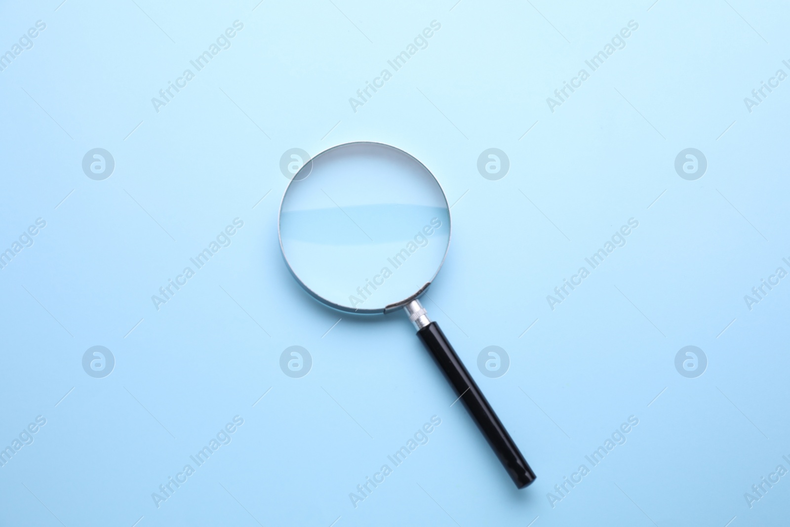 Photo of Magnifying glass on light blue background, top view