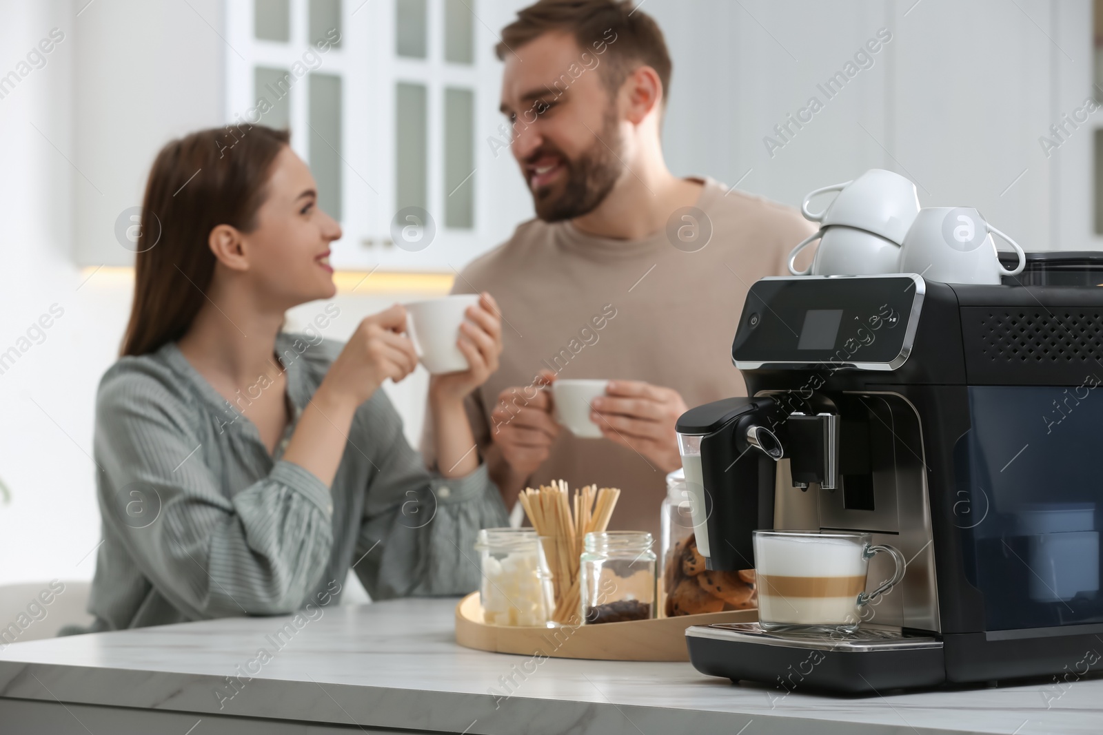 Photo of Happy couple enjoying fresh aromatic coffee in kitchen, focus on modern machine