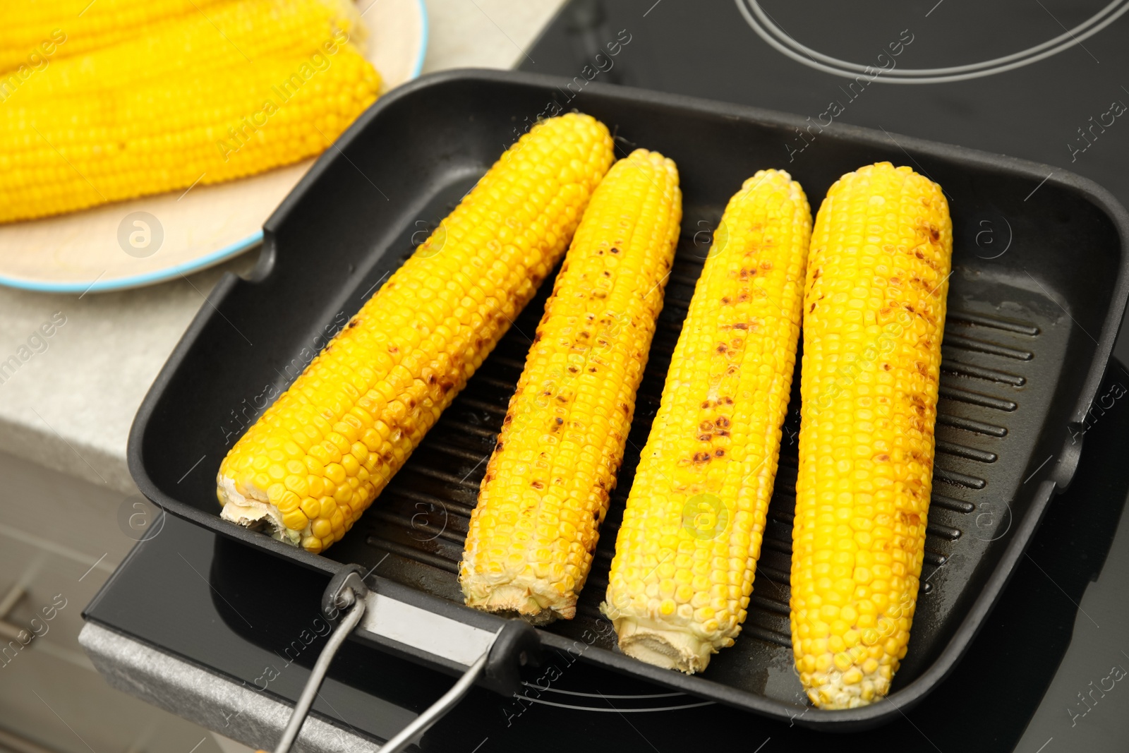 Photo of Cooking fresh corn cobs on grill pan, closeup