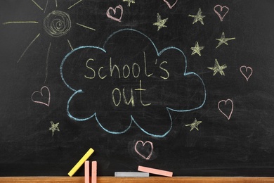 Photo of Pieces of color chalk near blackboard with text School's Out. Summer holidays
