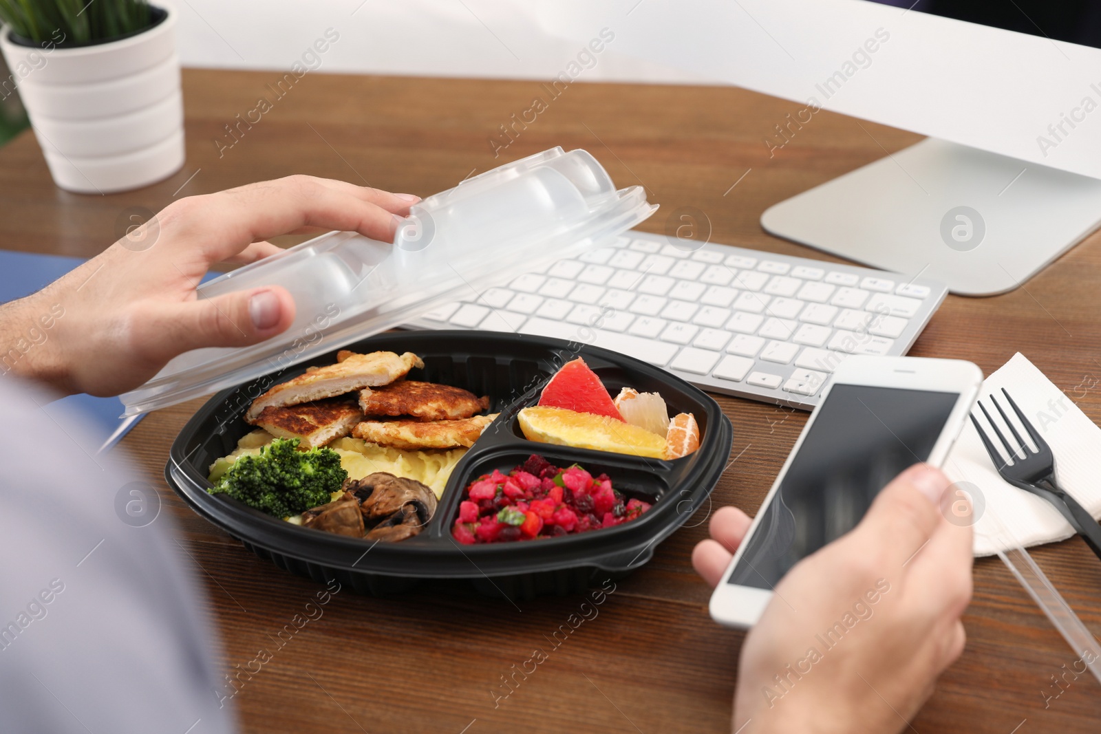 Photo of Office employee with smartphone having lunch at workplace, closeup. Food delivery