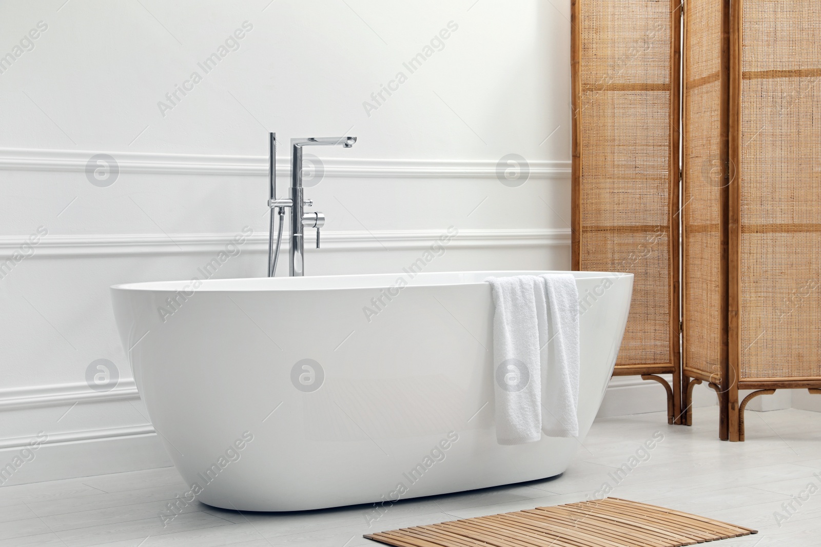 Photo of Modern ceramic bathtub and folding screen near white wall in room