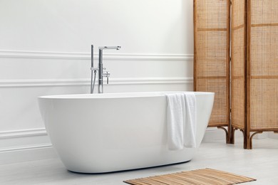 Photo of Modern ceramic bathtub and folding screen near white wall in room