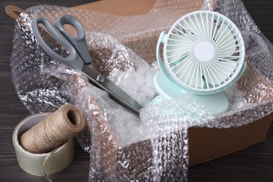 Photo of Small fan with bubble wrap in cardboard box and packaging items on dark wooden table