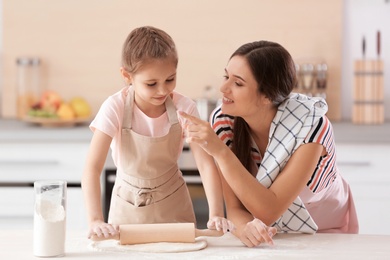 Mother and her daughter preparing dough at table in kitchen