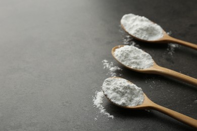 Photo of Baking powder in spoons on grey textured table, closeup. Space for text