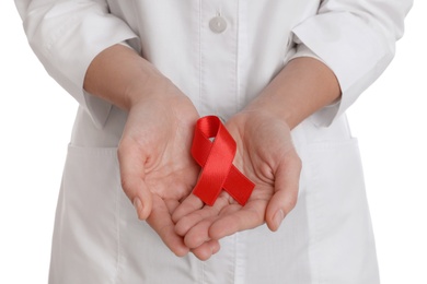Doctor holding red ribbon on white background, closeup. AIDS awareness month