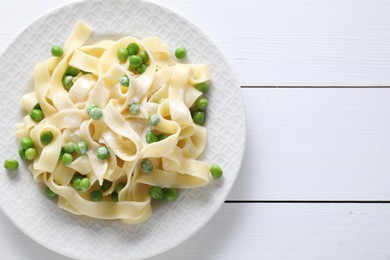 Photo of Delicious pasta with green peas on white wooden table, top view. Space for text