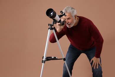 Senior astronomer looking at stars through telescope on brown background. Space for text