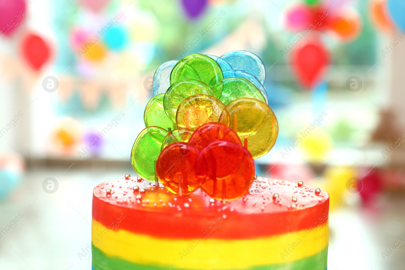 Photo of Bright birthday cake with candies in decorated room, closeup