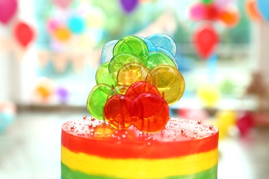 Bright birthday cake with candies in decorated room, closeup