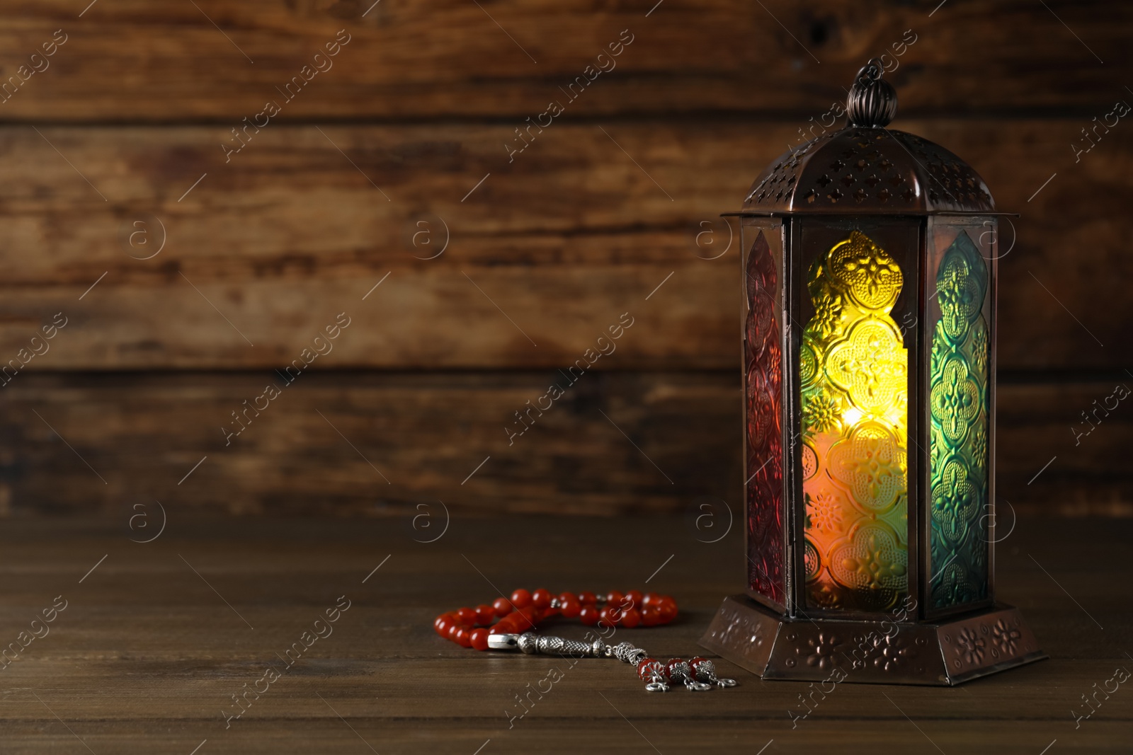 Photo of Decorative Arabic lantern and misbaha on wooden table. Space for text
