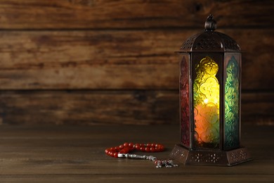 Photo of Decorative Arabic lantern and misbaha on wooden table. Space for text