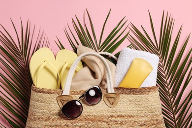 Flat lay composition with wicker bag, palm leaves and other beach accessories on pink background
