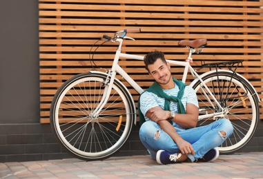 Photo of Handsome young hipster man with bicycle near wooden wall outdoors