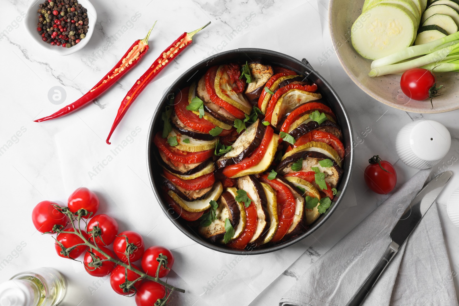 Photo of Delicious ratatouille, ingredients and knife on white table, flat lay