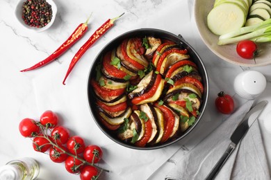 Delicious ratatouille, ingredients and knife on white table, flat lay