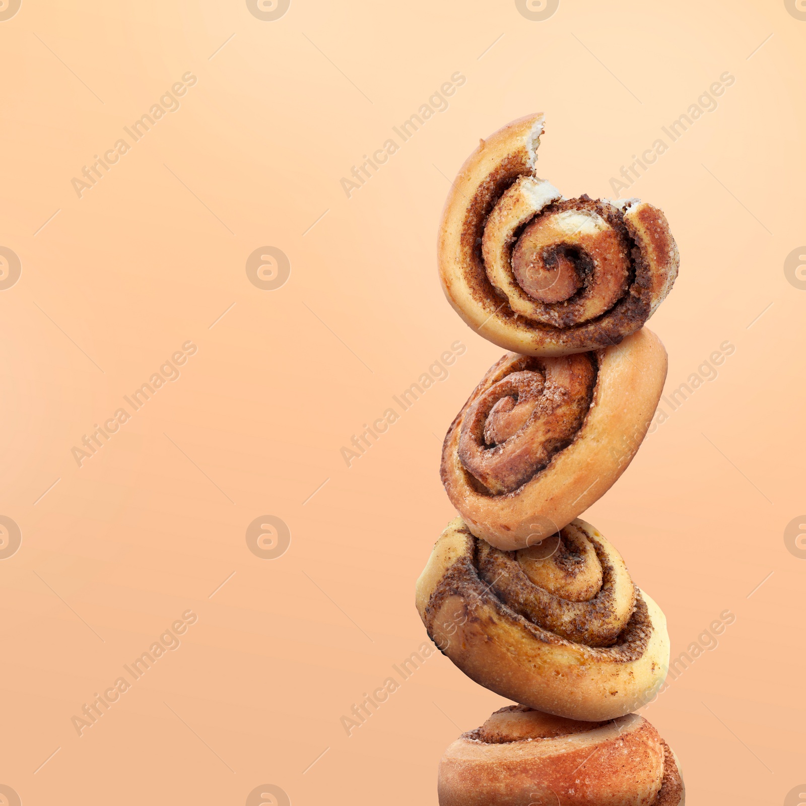 Image of Cinnamon rolls balancing on peach color background, space for text