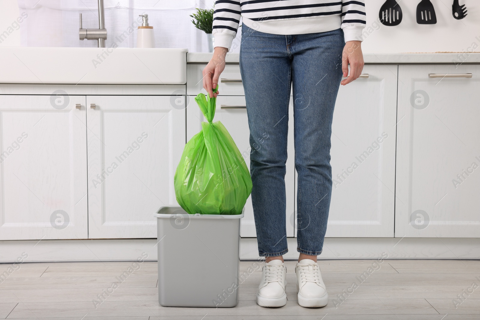 Photo of Woman taking garbage bag out of trash bin in kitchen, closeup