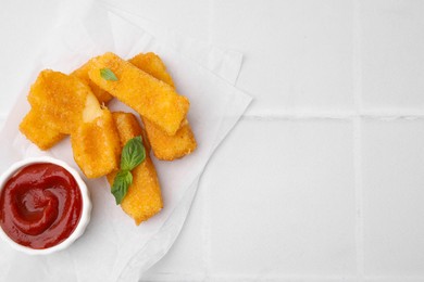 Photo of Tasty fried mozzarella sticks with basil leaves and ketchup on white tiled table, top view. Space for text