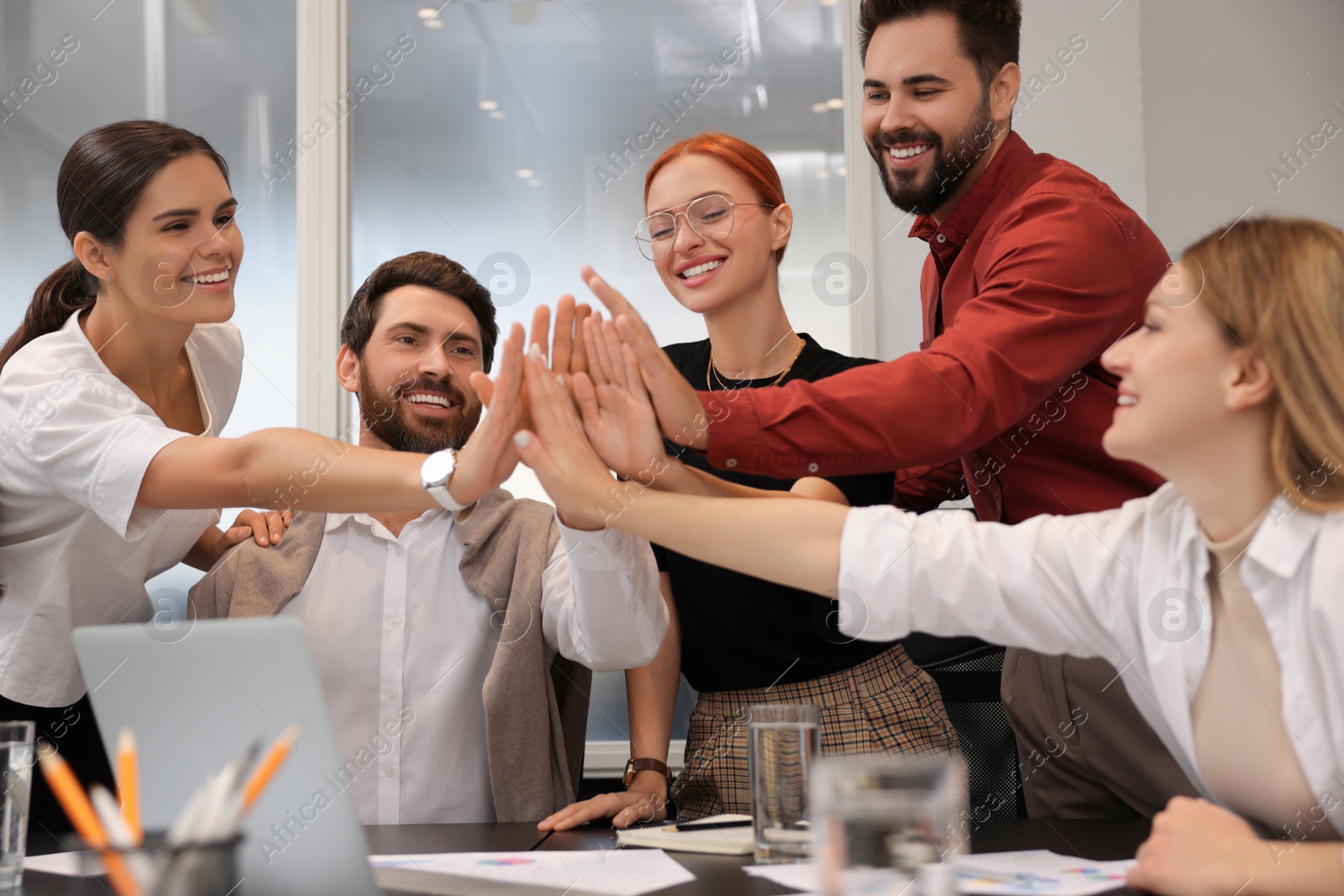 Photo of Team of employees joining hands in office