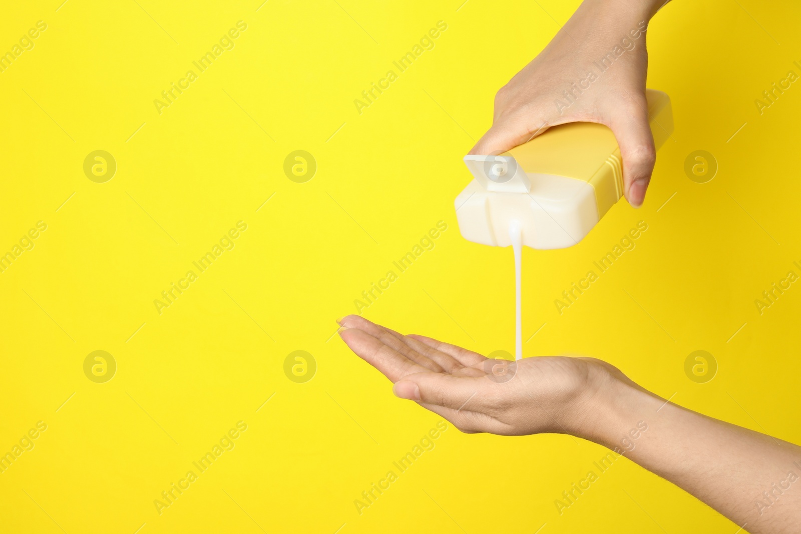 Photo of Woman pouring hair cosmetic product into hand on yellow background, closeup. Space for text