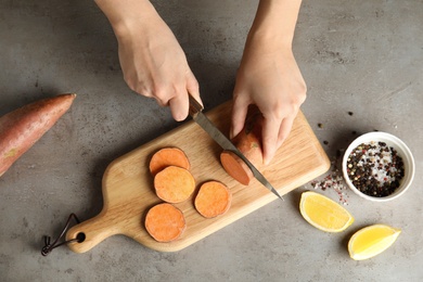 Photo of Woman cutting sweet potato on wooden board, top view