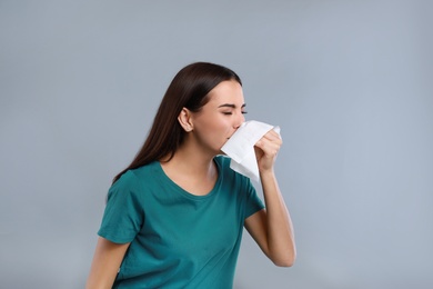 Young woman suffering from allergy on grey background