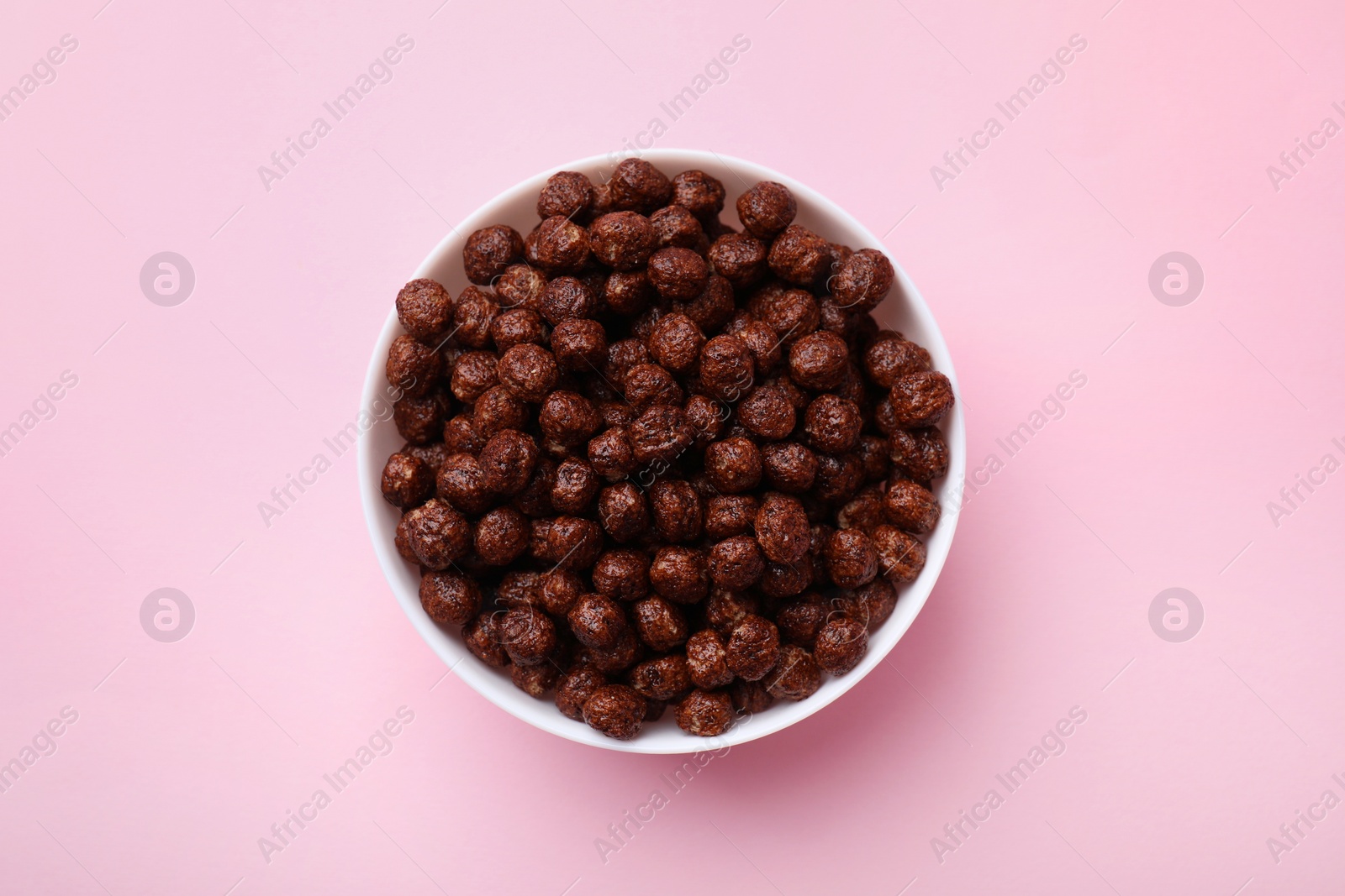 Photo of Chocolate cereal balls in bowl on pink table, top view