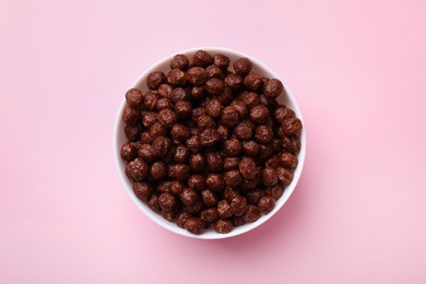 Photo of Chocolate cereal balls in bowl on pink table, top view