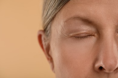 Woman with closed eyes on beige background, macro view. Space for text