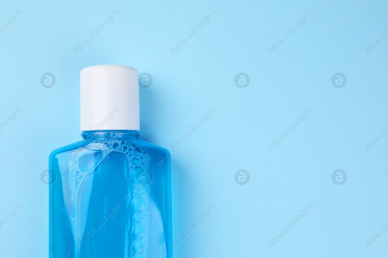 Photo of Fresh mouthwash in bottle on light blue background, top view. Space for text