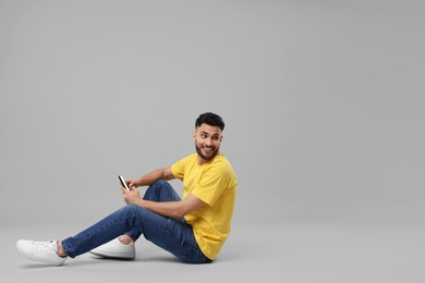 Photo of Happy young man using smartphone on grey background, space for text