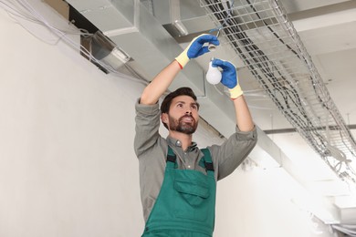 Photo of Professional electrician changing light bulb in room
