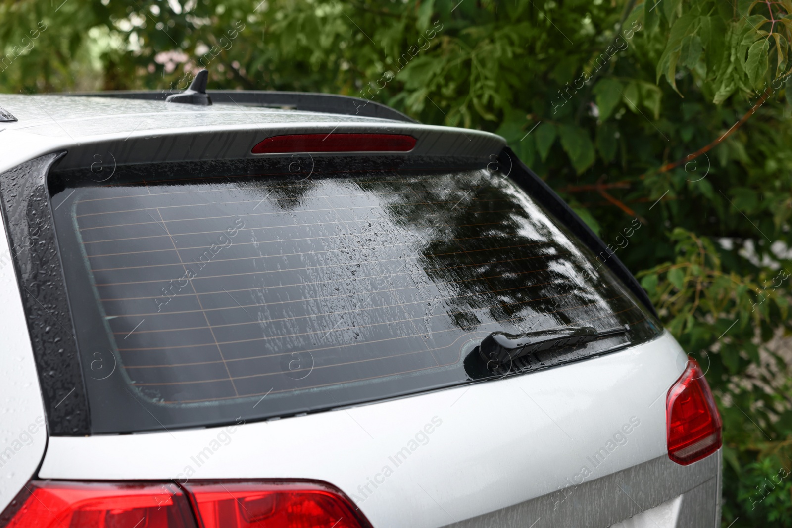 Photo of Wiper cleaning raindrops from car rear windshield outdoors