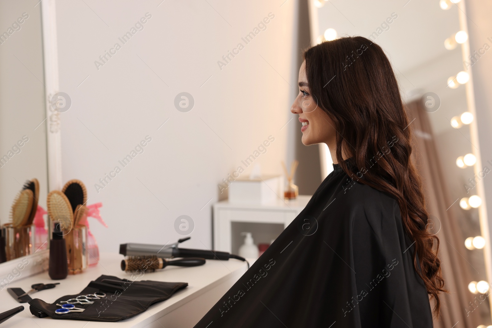 Photo of Smiling woman with curly hair sitting in salon. Space for text